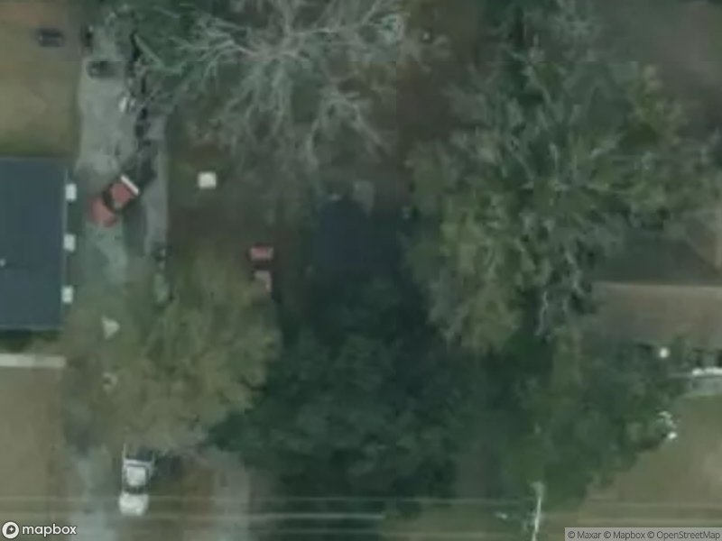 Aerial view of residential area with houses, trees, and parked vehicles.