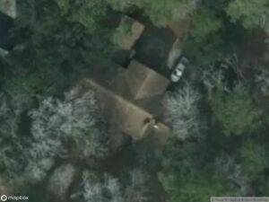 Aerial view of a house surrounded by trees, with a parked car visible.