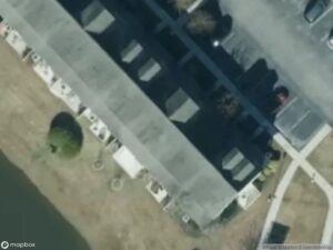 Aerial view of residential buildings, parking lot, and a small pond.