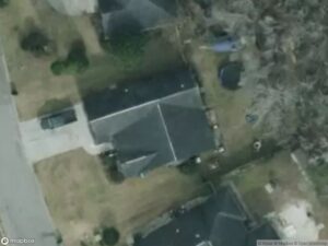 Aerial view of residential area with houses, driveways, and surrounding greenery.