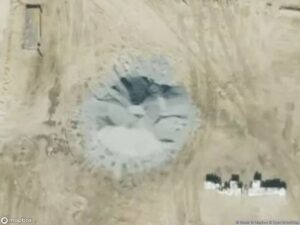 A circular area of disturbed soil with lighter and darker patches, surrounded by flat terrain.