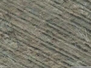 Aerial view of textured, plowed land with visible furrows and dry vegetation.