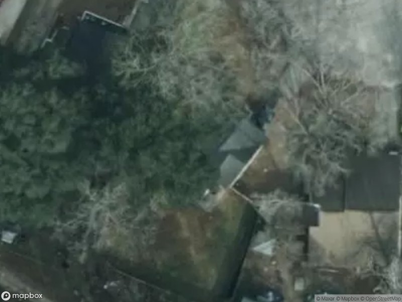 Aerial view of residential area with houses and trees. Ground is mostly bare.