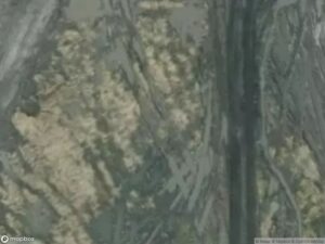 Satellite view showing varied terrain with dark and light patches, possibly indicating vegetation and bare ground.