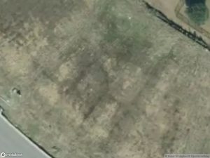 Aerial view of a grassy area with uneven terrain and a nearby road.
