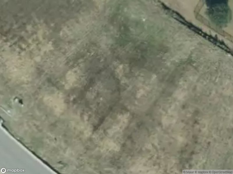 Aerial view of a grassy area with uneven terrain and a nearby road.