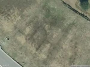 Aerial view of a grassy area with patches of bare soil and a road along the edge.