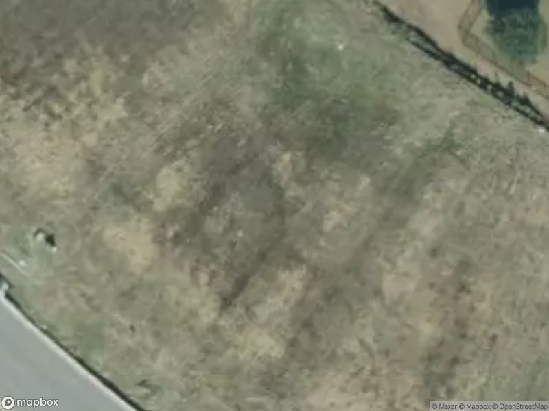Aerial view of a grassy area with patches of bare soil and a road along the edge.