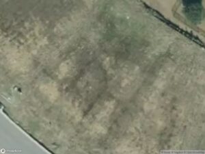 Aerial view of a grassy area with uneven terrain and a road along the edge.