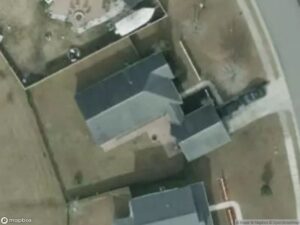 Aerial view of residential area with two houses, driveways, and surrounding yards.