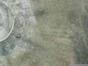 Aerial view of a circular structure surrounded by water and sandy terrain.