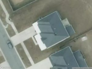 Aerial view of two houses with dark roofs and driveways, surrounded by bare land.