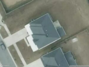 Aerial view of two houses with gray roofs and surrounding bare land.