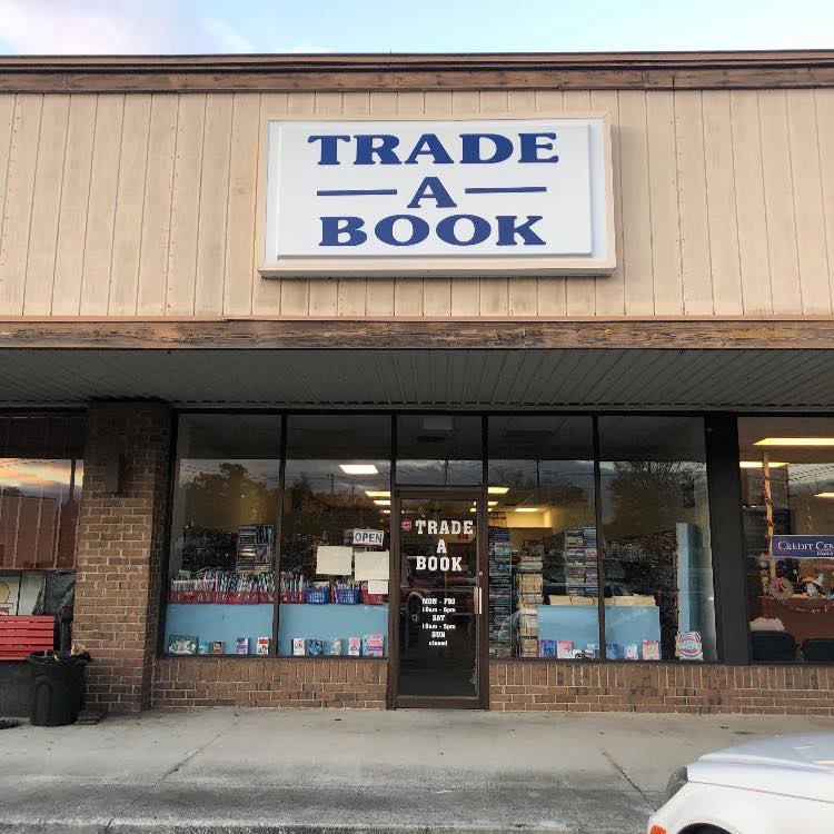 Bookstore exterior with a large sign reading "TRADE A BOOK" and visible shelves of books through the windows.