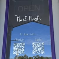 Sign on a shop window reads "The Nail Nook" with "Open" and QR codes for booking with Caitlyn or Nikki.