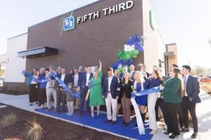 A group of people celebrates outside a Fifth Third Bank branch, holding a ribbon and posing for a photo.