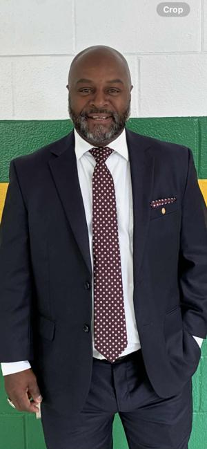 A man in a suit stands smiling against a green and yellow wall. He has a beard and a polka dot tie.