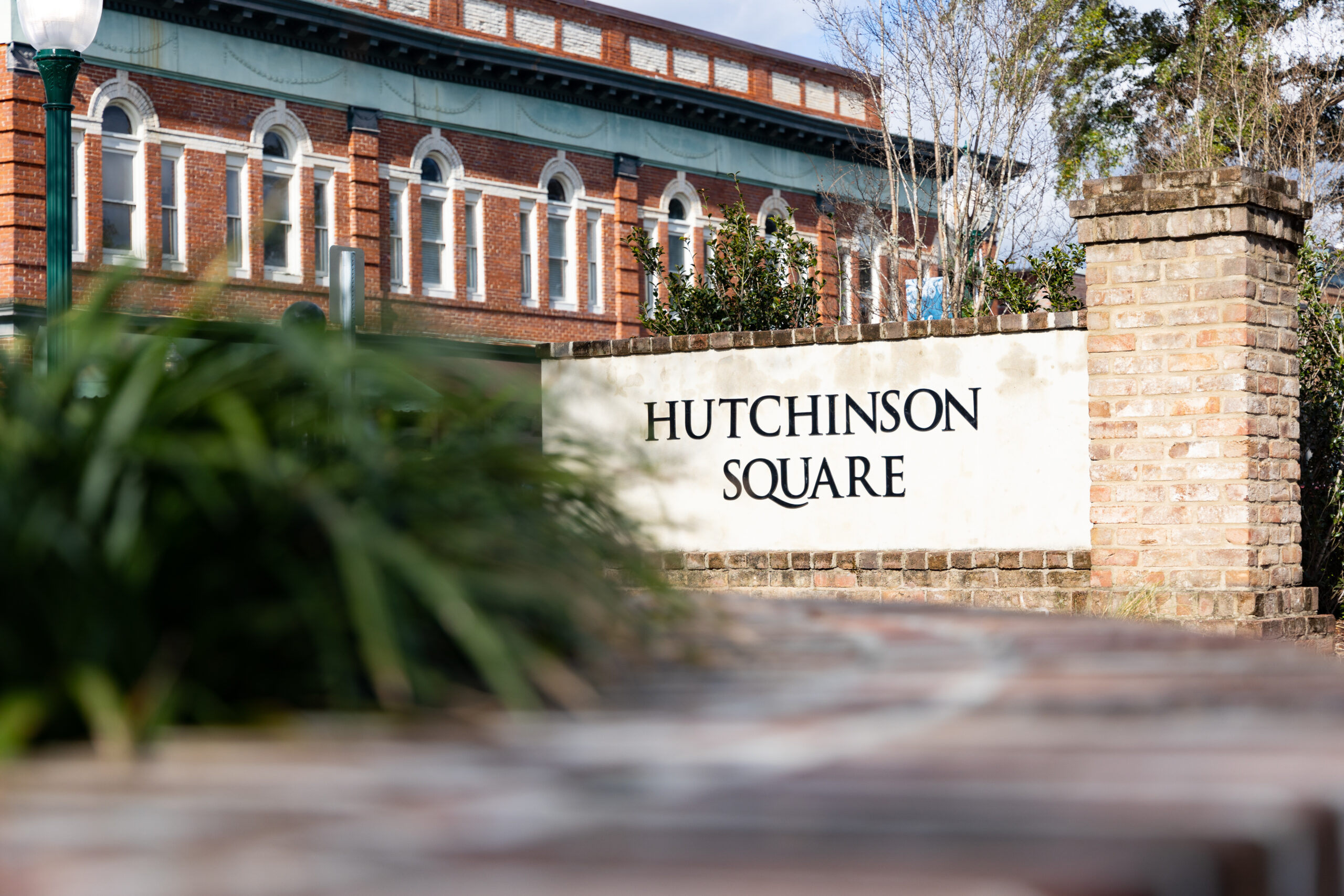 Sign for Hutchinson Square with brick border and greenery in foreground, historic building in background.