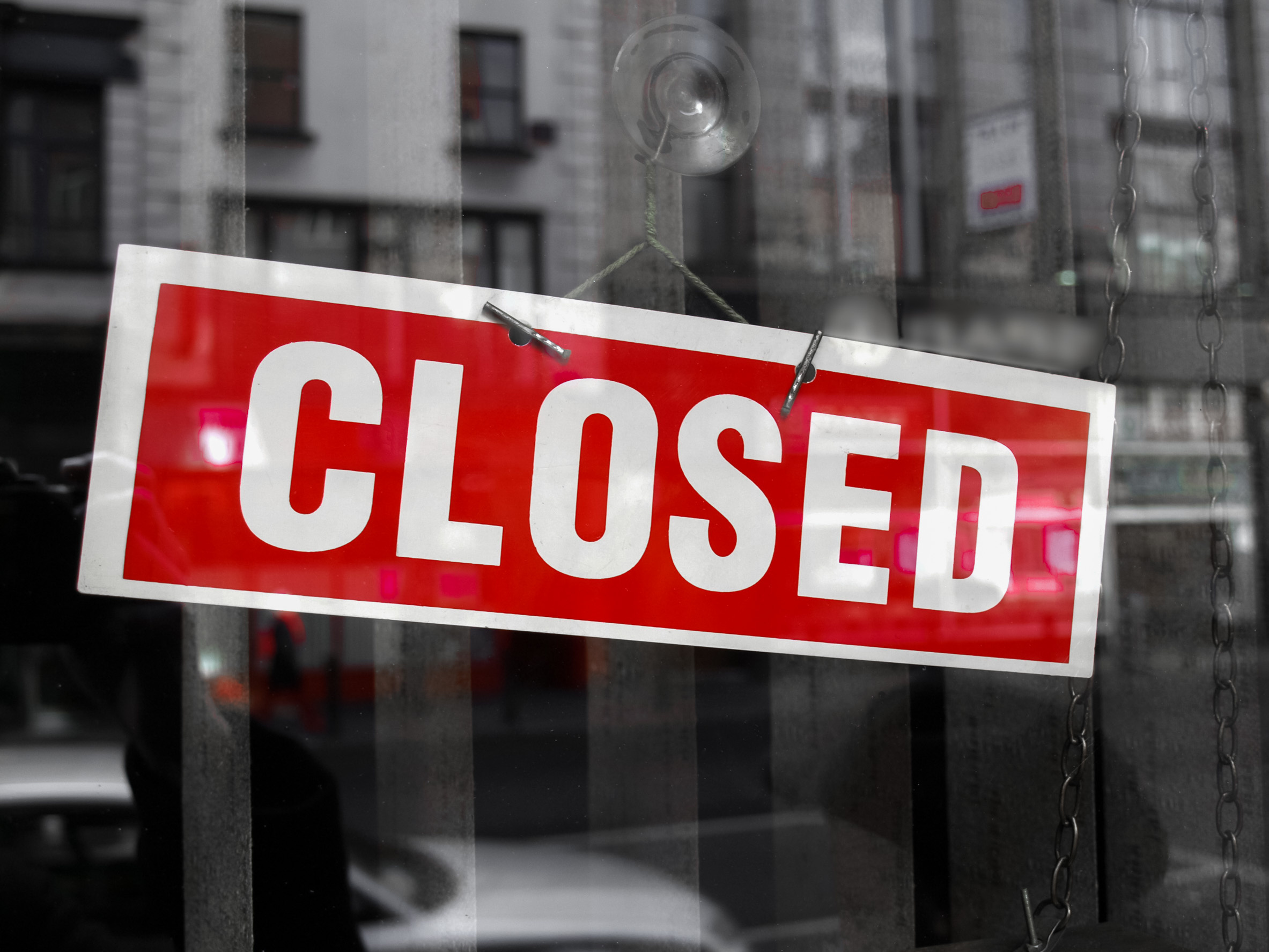 Red "CLOSED" sign hangs in a shop window, reflecting a desaturated urban background.