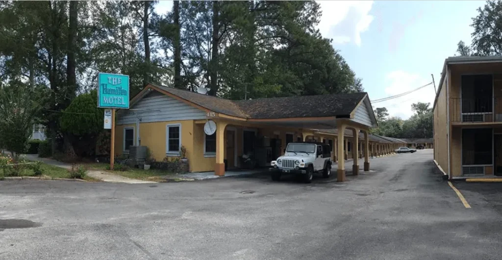 The Hamilton Motel features a yellow building with a sign, parked cars, and surrounding trees.