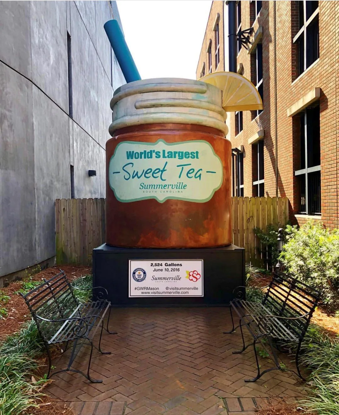 Giant sweet tea container with a straw and lemon slice, benches nearby, in Summerville, South Carolina.