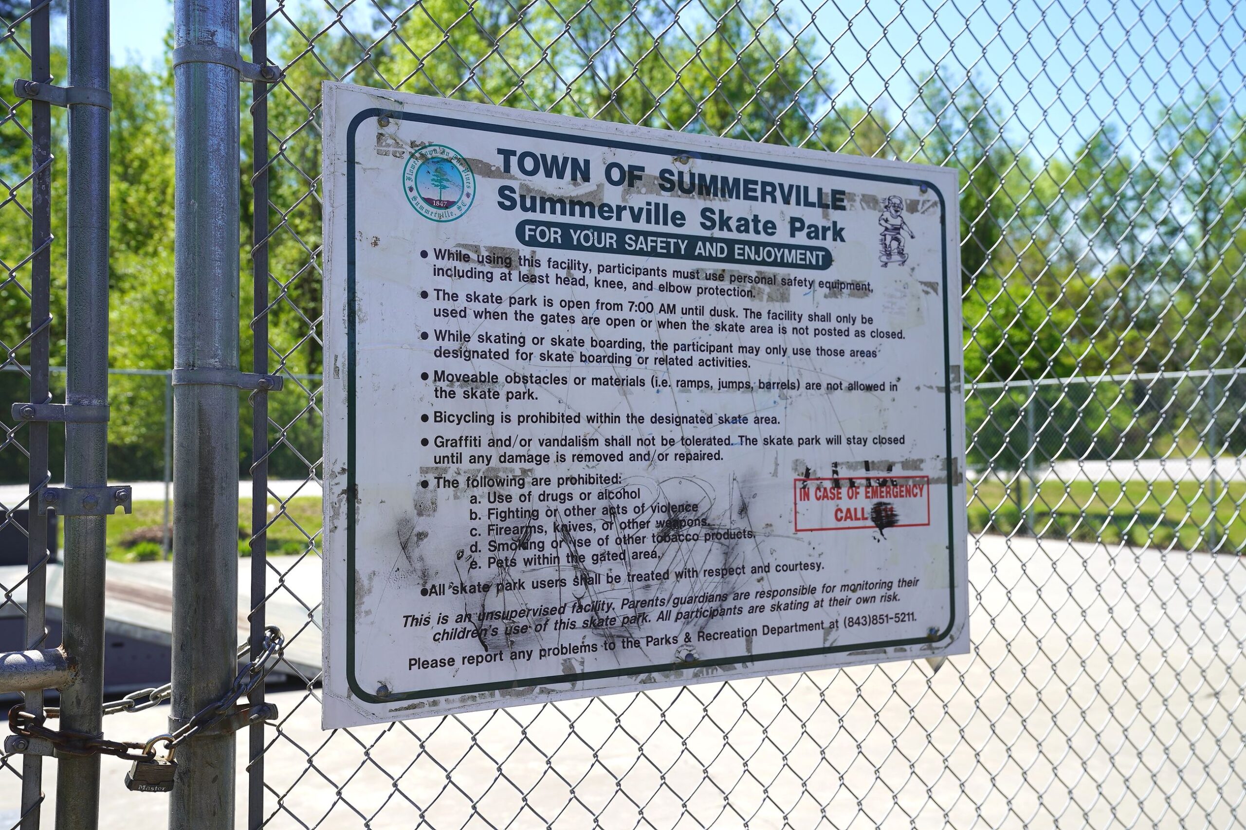 Sign at Summerville Skate Park outlines safety rules and regulations for users. Chain-link fence and park visible in background.