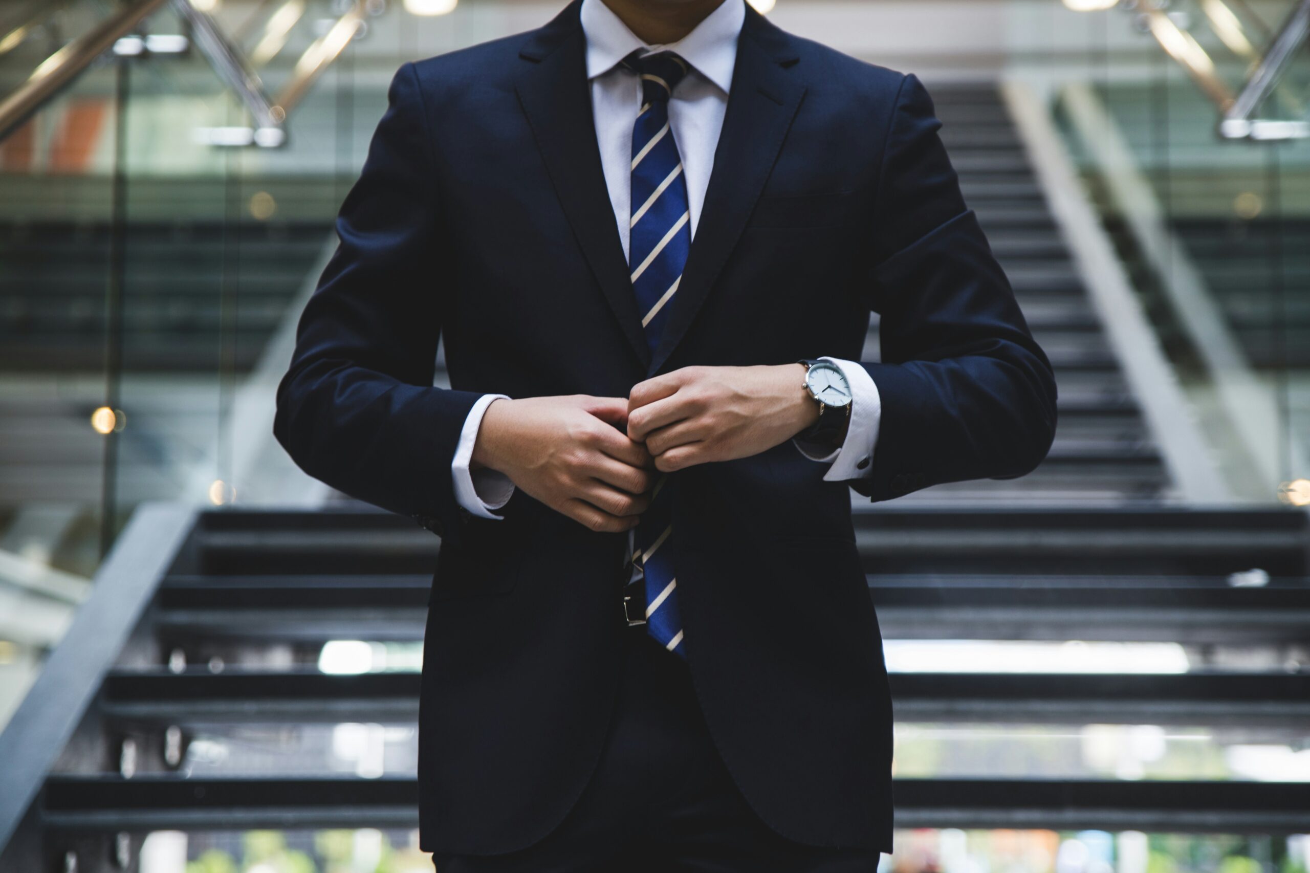 A person in a suit adjusts their tie while standing on stairs.