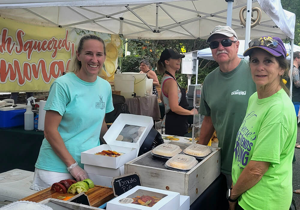 A vendor smiles at customers while showcasing fresh food items at a market stall.