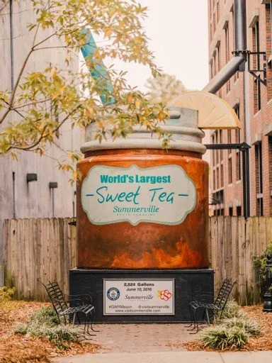 Giant replica of a sweet tea jar with a lemon slice, located in Summerville, surrounded by trees and benches.