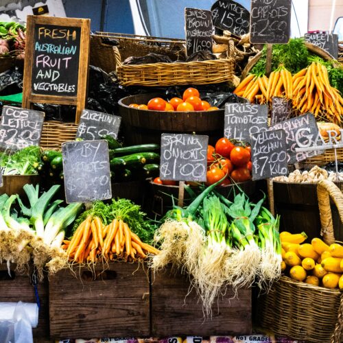A vibrant market display of fresh fruits and vegetables with price tags on wooden crates and baskets.