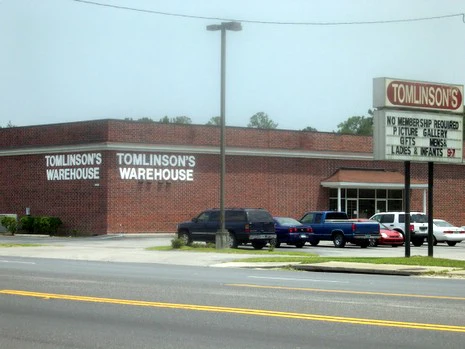 Tomlinson's Warehouse building with a sign advertising gifts and a picture gallery. Several parked cars visible.