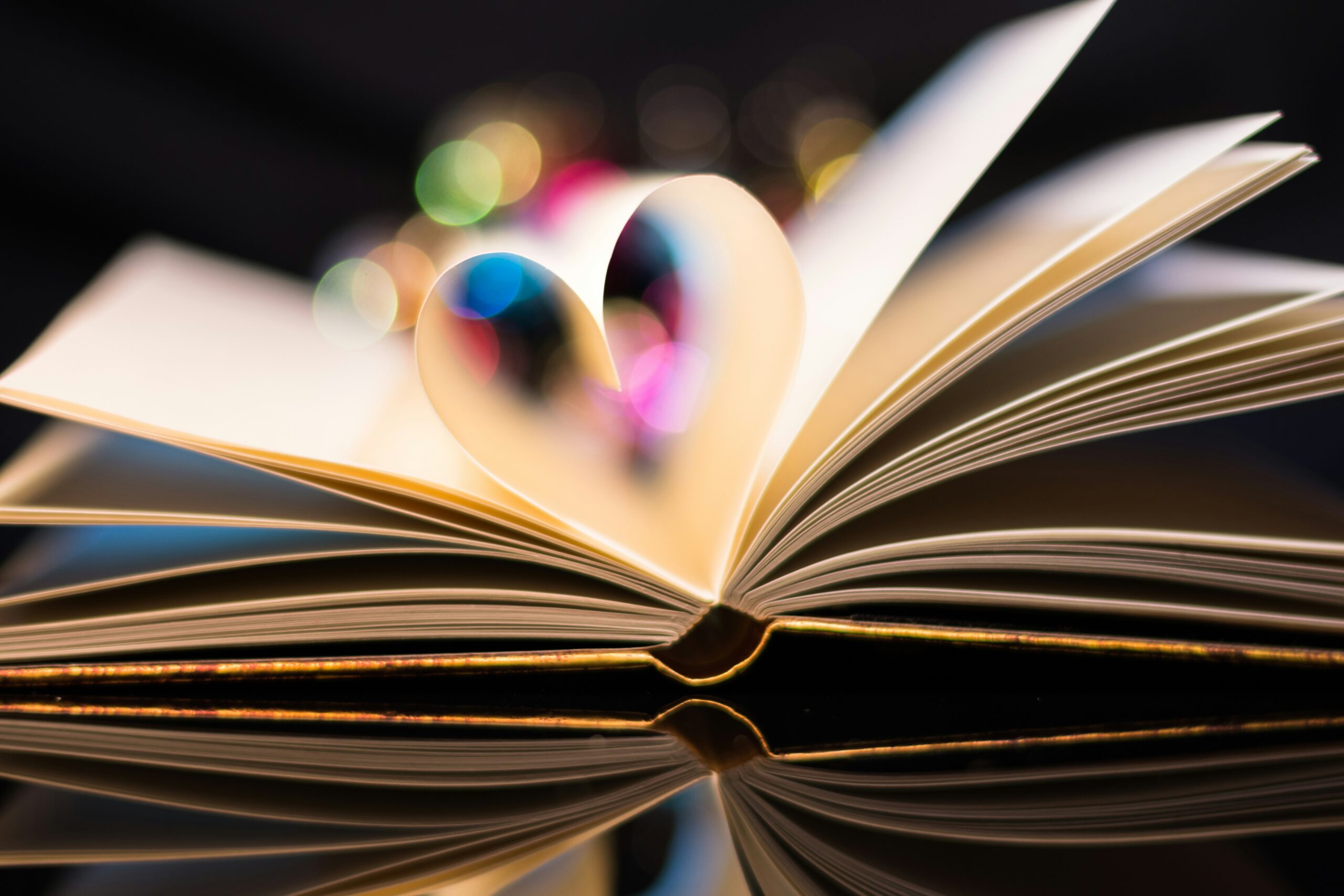 An open book with a heart-shaped page, reflecting colorful bokeh lights in the background.