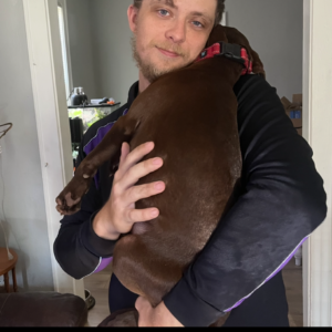 A person holds a brown dog close, smiling gently in a home setting.