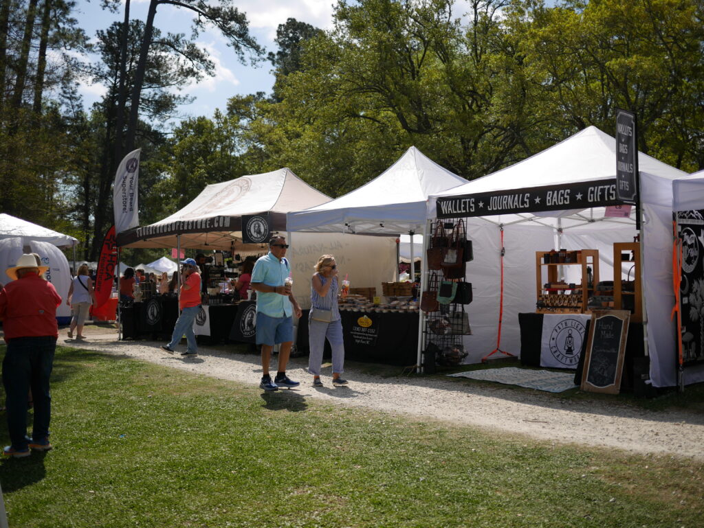 People browse vendor tents at an outdoor market, showcasing various handmade goods and crafts.