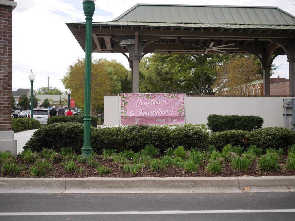 A banner announces a countdown to an event, surrounded by greenery and a gazebo structure.