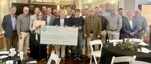 A group of people poses together, holding a large check at a dining event.
