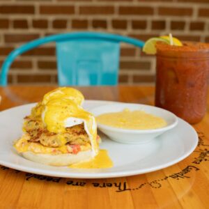 Plate with two poached eggs on crab cakes, topped with hollandaise sauce, served with grits and a drink.