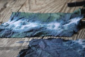 Textured fabric pieces in shades of blue and green lie on a wooden surface.