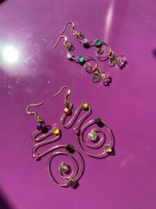 Two pairs of colorful, spiral-shaped earrings with beads on a purple surface.