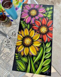 Colorful painting of three large flowers—pink, red, and yellow—surrounded by green leaves on a black background.