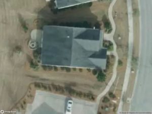 Aerial view of a house with a driveway and landscaped yard. Surrounding roads are visible.