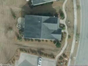 Aerial view of a house with a driveway, surrounded by landscaping and a curved road.
