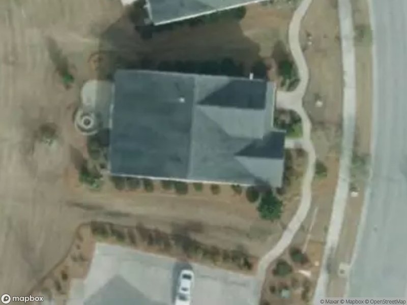 Aerial view of a house with a driveway, surrounded by landscaping and a curved road.
