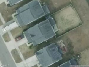 Aerial view of residential homes with yards and parked cars on a suburban street.