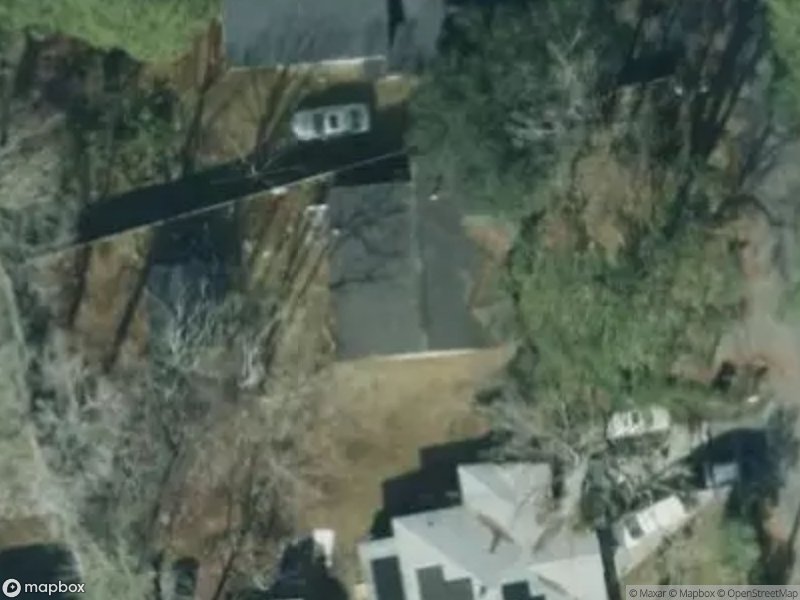 Aerial view of residential area with houses, trees, and a parked vehicle on a driveway.