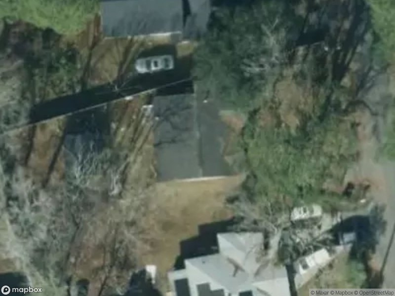Aerial view of residential area with houses, trees, and a parked car on a driveway.