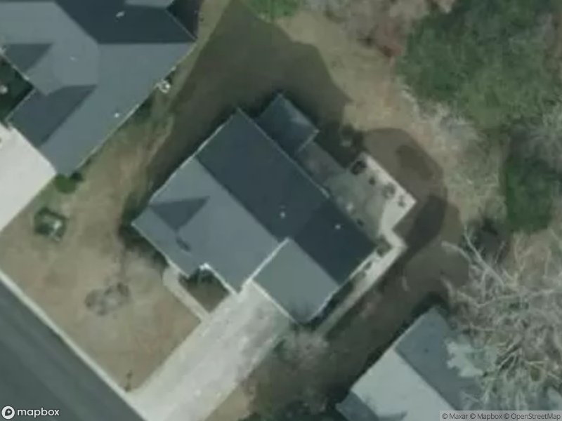 Aerial view of two houses with dark roofs and driveways, surrounded by grass and trees.