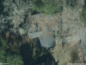 Aerial view of a house surrounded by trees and overgrown vegetation.
