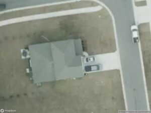 Aerial view of a house with a driveway and two parked cars on a residential street.
