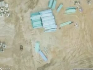 Aerial view of construction materials, including stacked pipes and scattered items on a sandy surface.